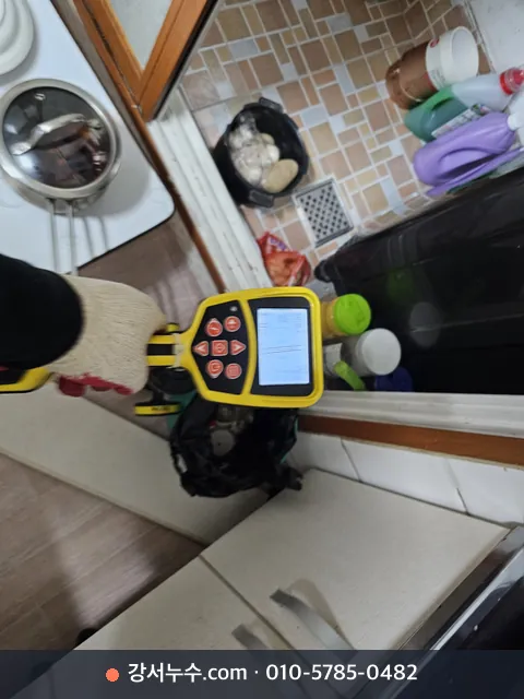 주방 바닥에서 휴대용 탐지기 화면을 보며 배관 위치를 확인