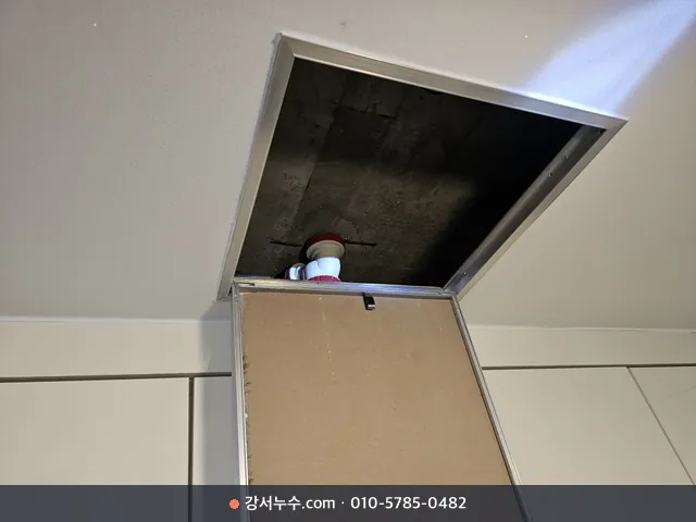 욕실 천장 점검구를 열어 위층 배관 아래를 확인하는 장면